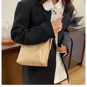 Detail of a beige patent leather crescent shoulder bag with high-gloss finish on a model