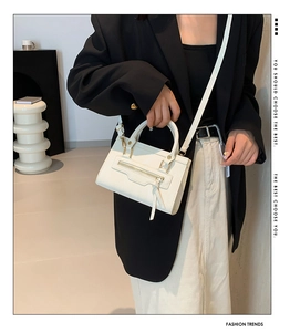 Detailed view of a white leather crossbody bag with zipper accent on a model