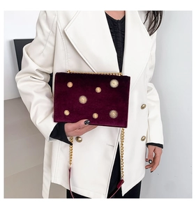 Detail of burgundy velvet crossbody bag with golden floral studs and chain strap