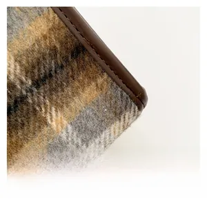 Detail of plaid wool fabric and brown leather piping on a structured crossbody bag