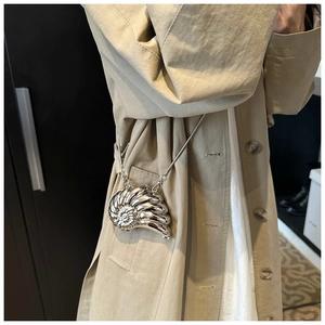 Silver shell-shaped mini bag with chain strap shown as crossbody on trench coat