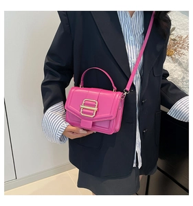 Detail of fuchsia leather crossbody bag with bold gold buckle and handle on striped shirt