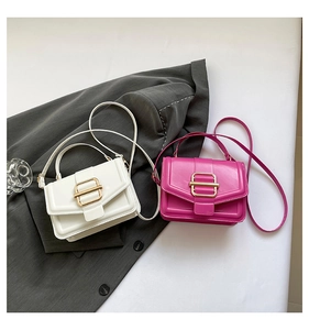Flat lay of white and plum purple square handbags with gold buckles on grey blazer