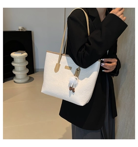 Detail of white embossed leather tote bag with pattern and plush charm on model