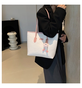 Detail of white embossed tote bag with pink trim and cute plush cartoon keychain