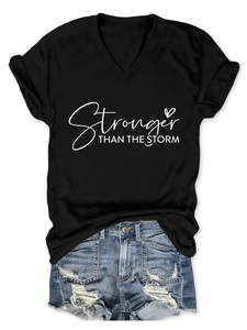 Dettaglio flat lay della maglietta nera con scollo a V e scritta Stronger Than The Storm