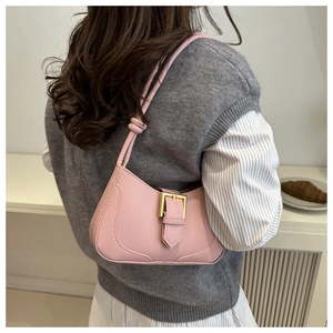 Détail d'un sac hobo en cuir rose clair porté à l'épaule avec une boucle dorée