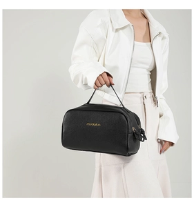 Detail of black lychee grain leather handbag with gold logo and dual zippers on white outfit