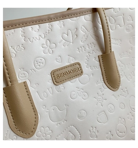 Detailed macro view of white leather tote with embossed love patterns and brand logo tag