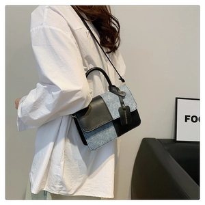 Detail showing blue denim and black leather contrast stitching on the shoulder bag