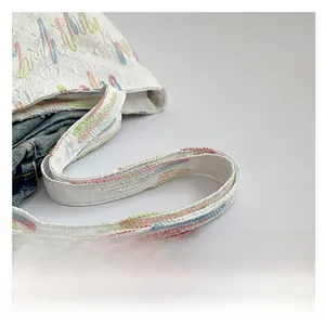 Close-up of white tote bag strap with colorful embroidery and quilted stitching detail