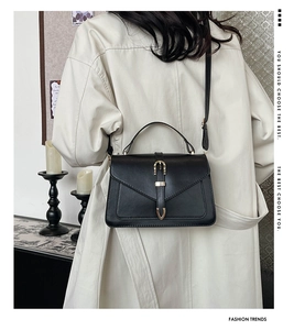 Détail d'un sac bandoulière chic en cuir noir avec boucle dorée sur un manteau clair