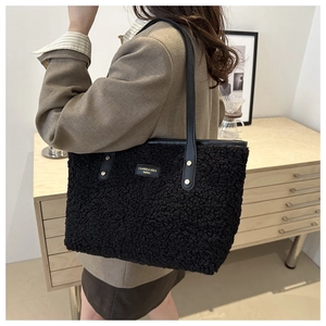 Close-up of black fuzzy tote bag with leather strap and gold logo plate for women