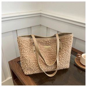 Close-up of cozy teddy fleece tote bag with leather trim and logo on glass table