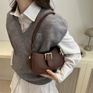 Sac à bandoulière en cuir marron avec boucle dorée et détail de nœud porté par un modèle