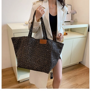 Model wearing a large leopard print canvas tote bag with brown leather patch detail