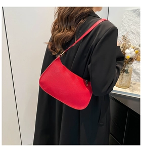 Detail of red leather baguette bag worn over the shoulder with a dark coat