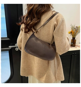 Detail of dark brown leather baguette bag with litchi texture and gold hardware on model