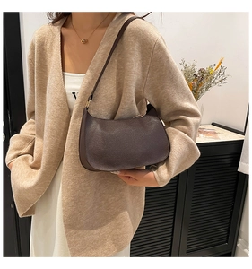Detail of dark brown leather baguette bag with litchi texture on a model in beige knitwear