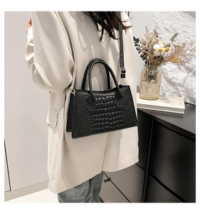 Detail of black faux crocodile leather bag with gold buckle on a beige blazer background