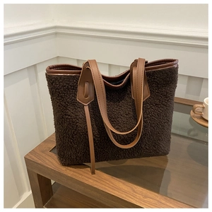 Detail of dark coffee faux shearling tote bag with brown leather handles on wooden table