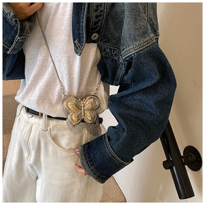 Détail du mini sac papillon métallisé avec chaîne porté sur une veste en jean
