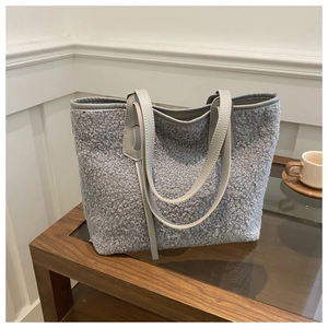 Detail of grey fuzzy lamb wool tote bag with PU leather handles on a wooden table
