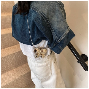 Gros plan d'un mini sac papillon en métal argenté avec chaîne sur une veste en jean