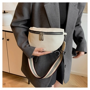 Détail d'un sac selle en cuir blanc avec bandoulière rayée et fermetures éclair argentées