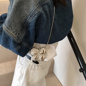 Mini sac papillon argenté avec chaîne porté par un mannequin sur une veste en jean
