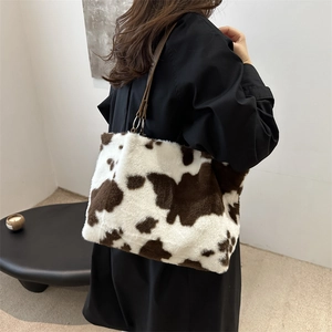 Minimalist cow print faux fur tote bag with brown leather straps worn by a female model