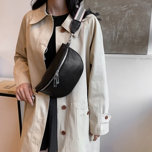 Sac bandoulière demi-lune noir avec large sangle rayée porté sur un trench-coat