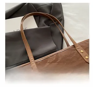Detail of dark brown tote bag showing pleated texture and gold rivets on the handle