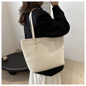 Detail of a creamy white tote bag with gold rivets and wrinkled leather texture on a model