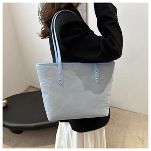 Detail of light blue pleated tote bag showing slim double straps and gold rivet accents