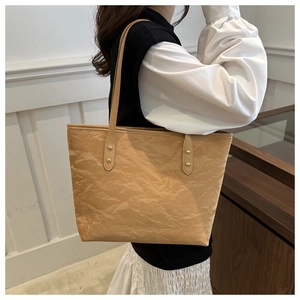 Detail of light camel tote bag with wrinkled texture and slim shoulder straps on a model