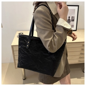 Detail of vintage black pleated tote bag with golden rivets shown in a lifestyle setting