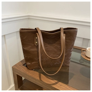 Detail of dark brown tote bag featuring unique pleated texture and gold metallic rivets