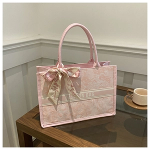 Detailed view of pink patterned fabric tote bag with silk scarf and logo on wooden table