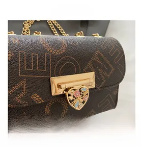 Detail of golden metal clasp and heart pendant on monogrammed crossbody bag