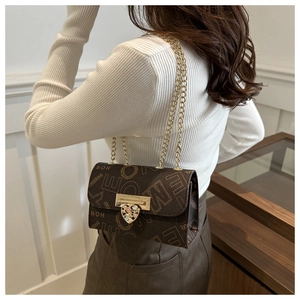 Detail of brown leather chain bag with gold heart clasp worn by model for elegant style