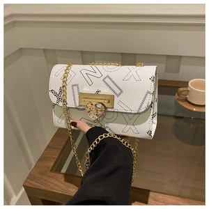 Detail of white leather crossbody bag featuring heart-shaped gold clasp and chain strap