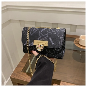 Detail of black pebbled crossbody bag with golden chain and heart-shaped enamel clasp