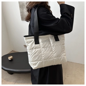 Sac fourre-tout matelassé blanc crème avec poignées en nylon noir porté par un mannequin