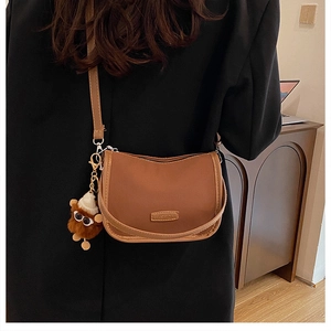 Detail view of brown vintage crossbody bag with fashion label and plush monkey charm