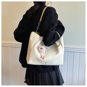 Detail of a large cream tote bag with brown handles and a pink plush monster charm