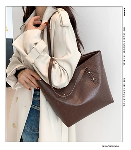 Detail of a large brown crocodile-pattern tote bag with gold rivets worn by a model