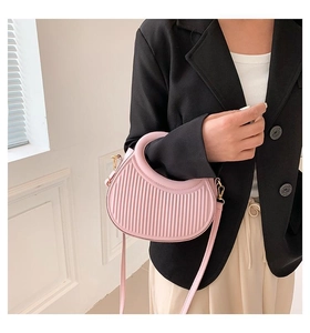 Detail of pink pleated handbag with gold ring handle and strap on model's black suit