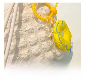 Detail of cream puff textured handbag with bright yellow floral charm and plastic chain
