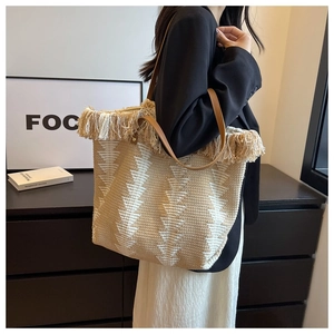 Close-up of woven bucket bag featuring bohemian fringe trim and leather shoulder straps